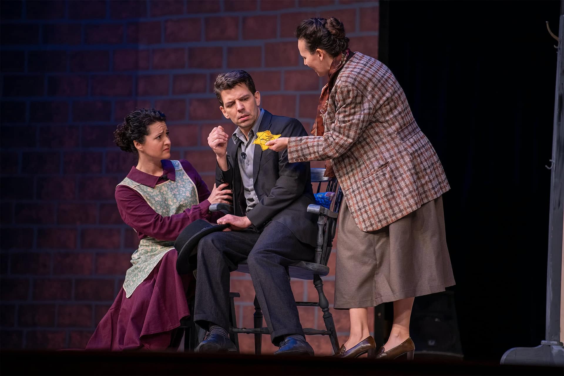 Two women talking to a man wearing black and sitting in a chair. 