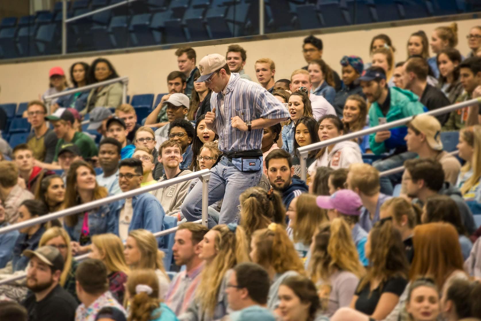 Students sitting in the bleachers while one male student runs down the steps at their senior class party.