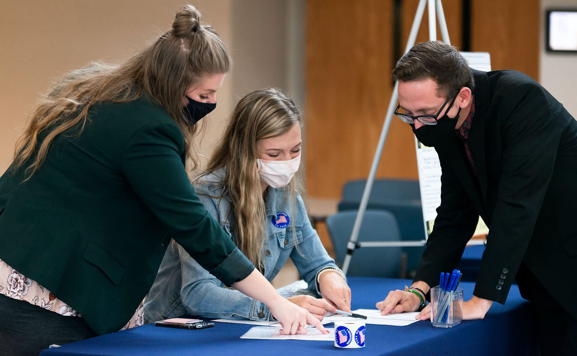 Two female volunteers showing a male student how to register to vote.