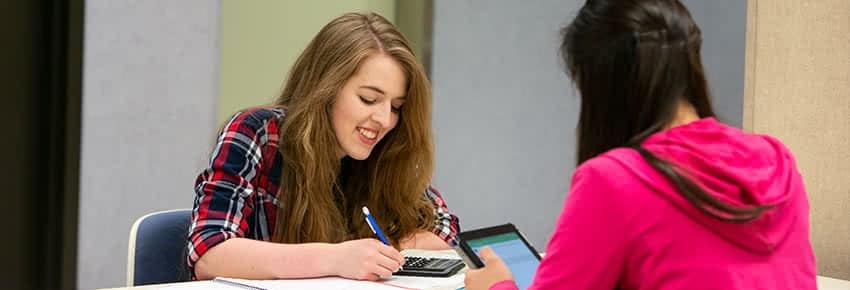 Two female students sitting at a table and working on assignments.