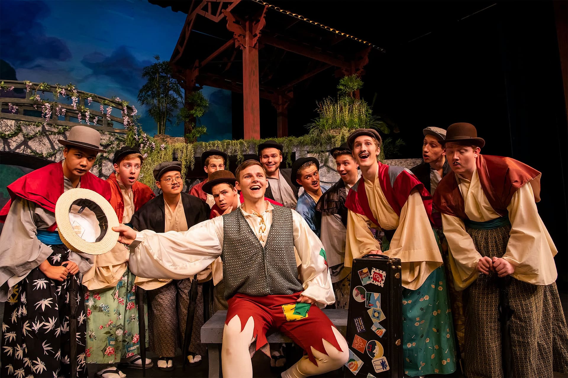 Men gathered around a man wearing a vest and holding a hat.