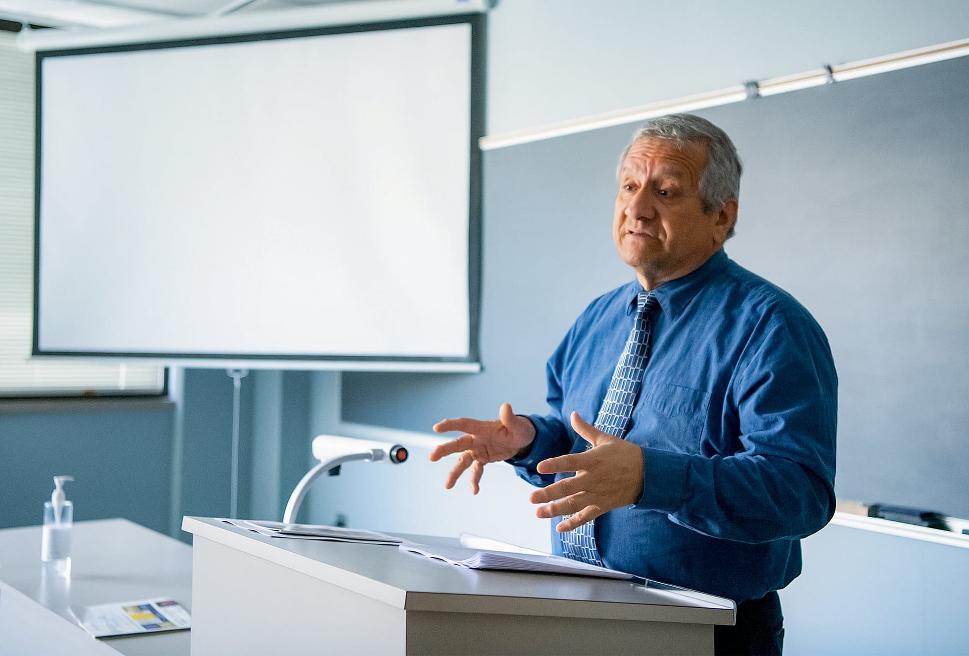 Professor standing at the classroom podium and speaking to his class.