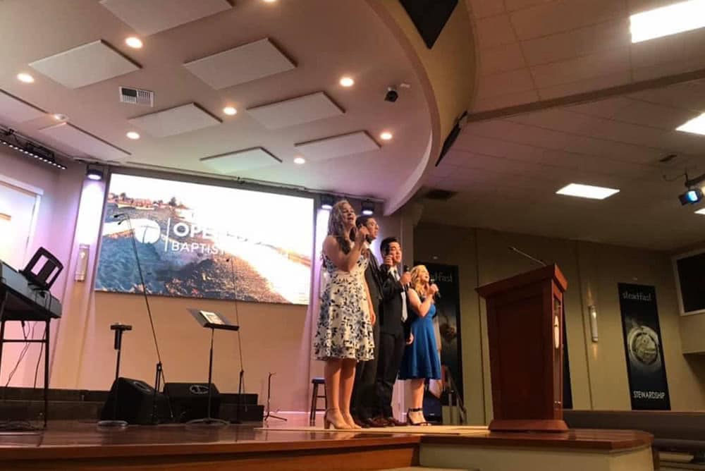 Proclaim singers standing on a church stage and signing. 
