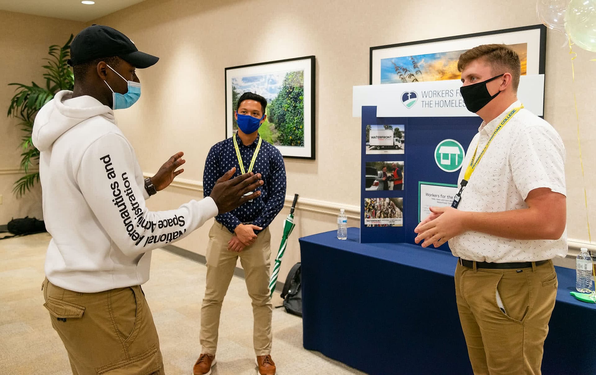 Three guys discuss joining the "Workers for the Homeless" Christian service group at the Christian Service expo