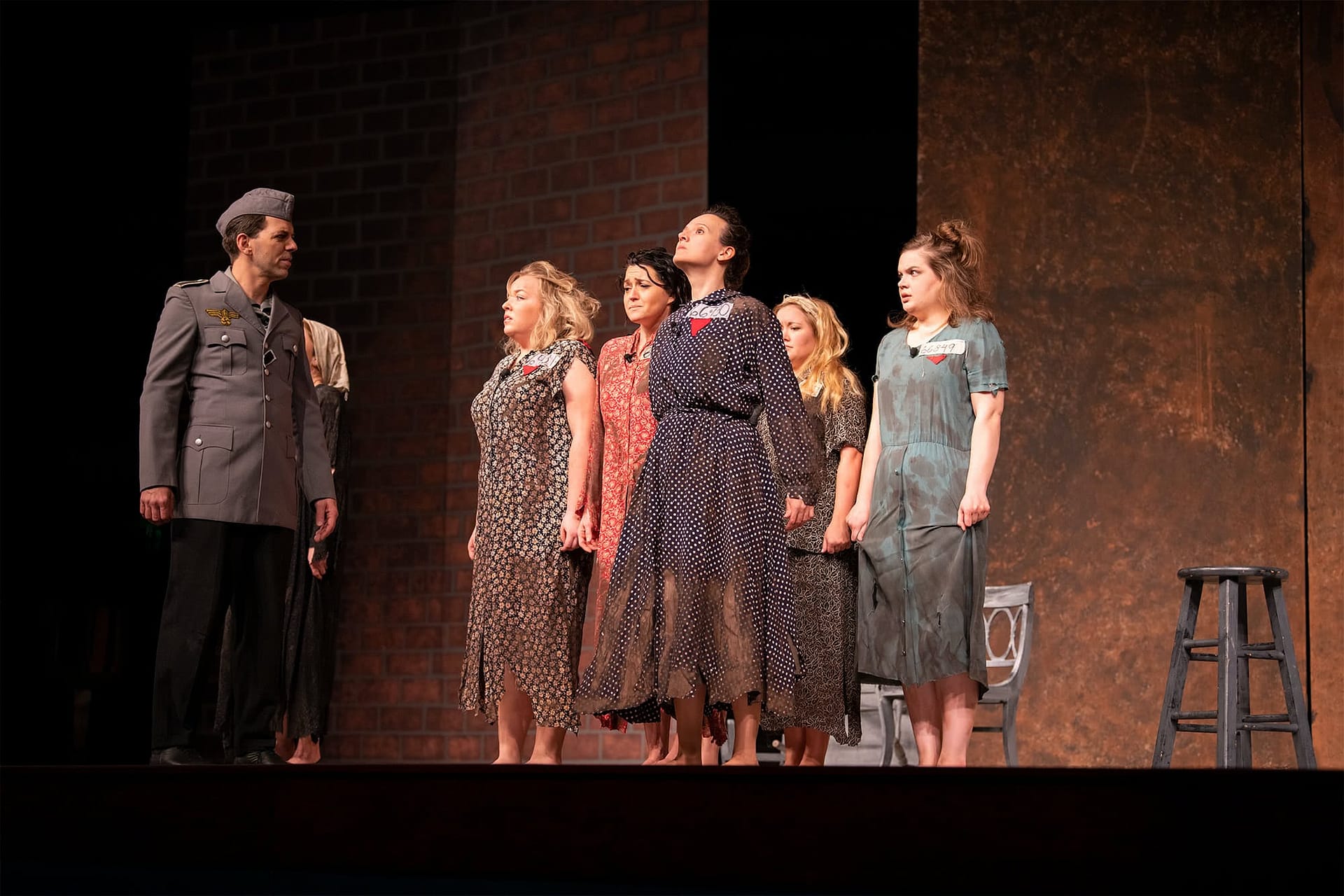 A man in a military uniform looking at five women standing in ragged dresses. 