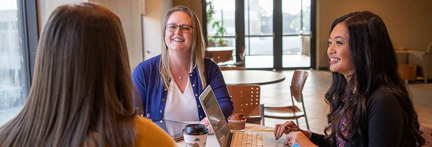 Three women sitting together at a table in the PCC Commons.