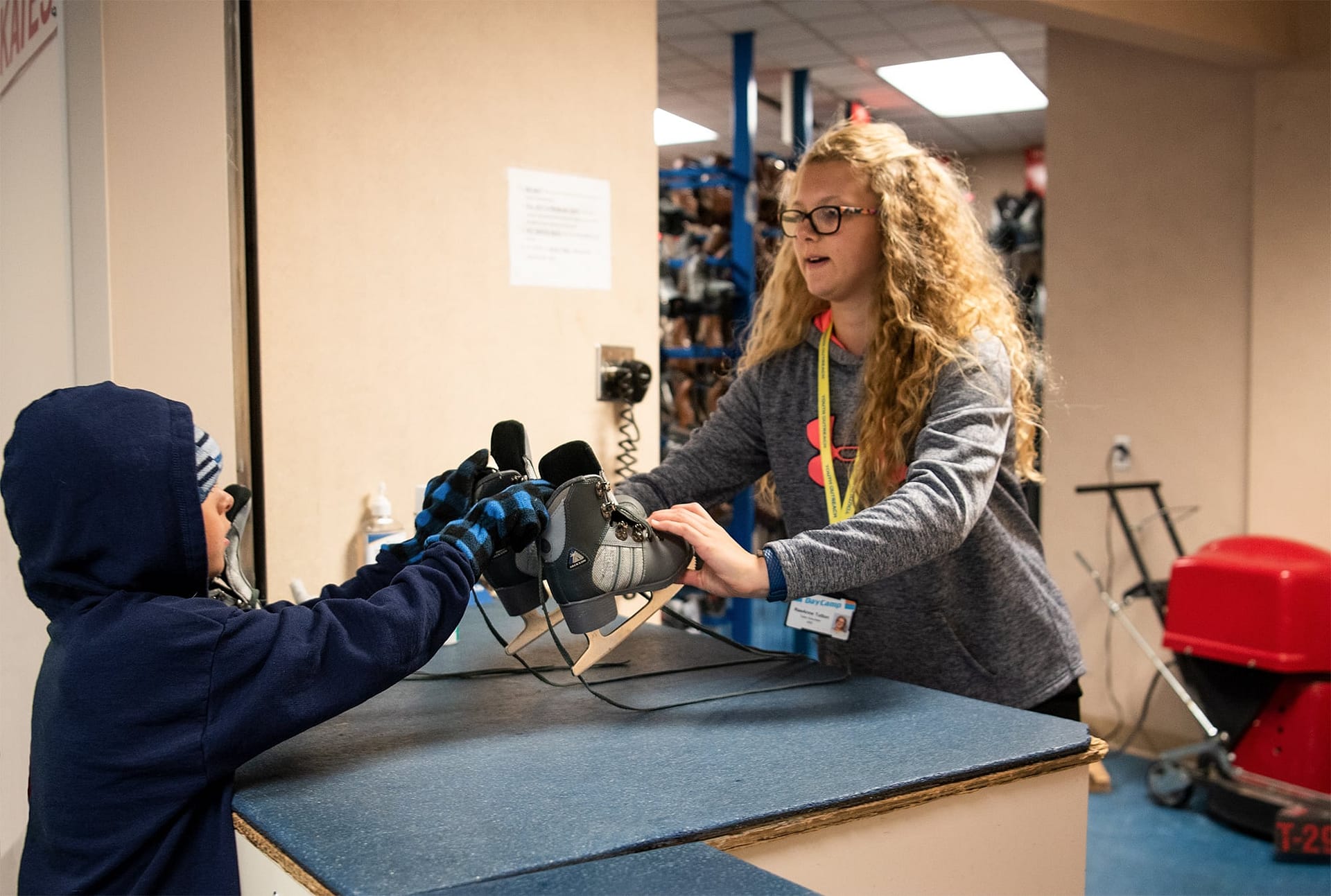 Day Camp helper handing ice skates to a camper. 