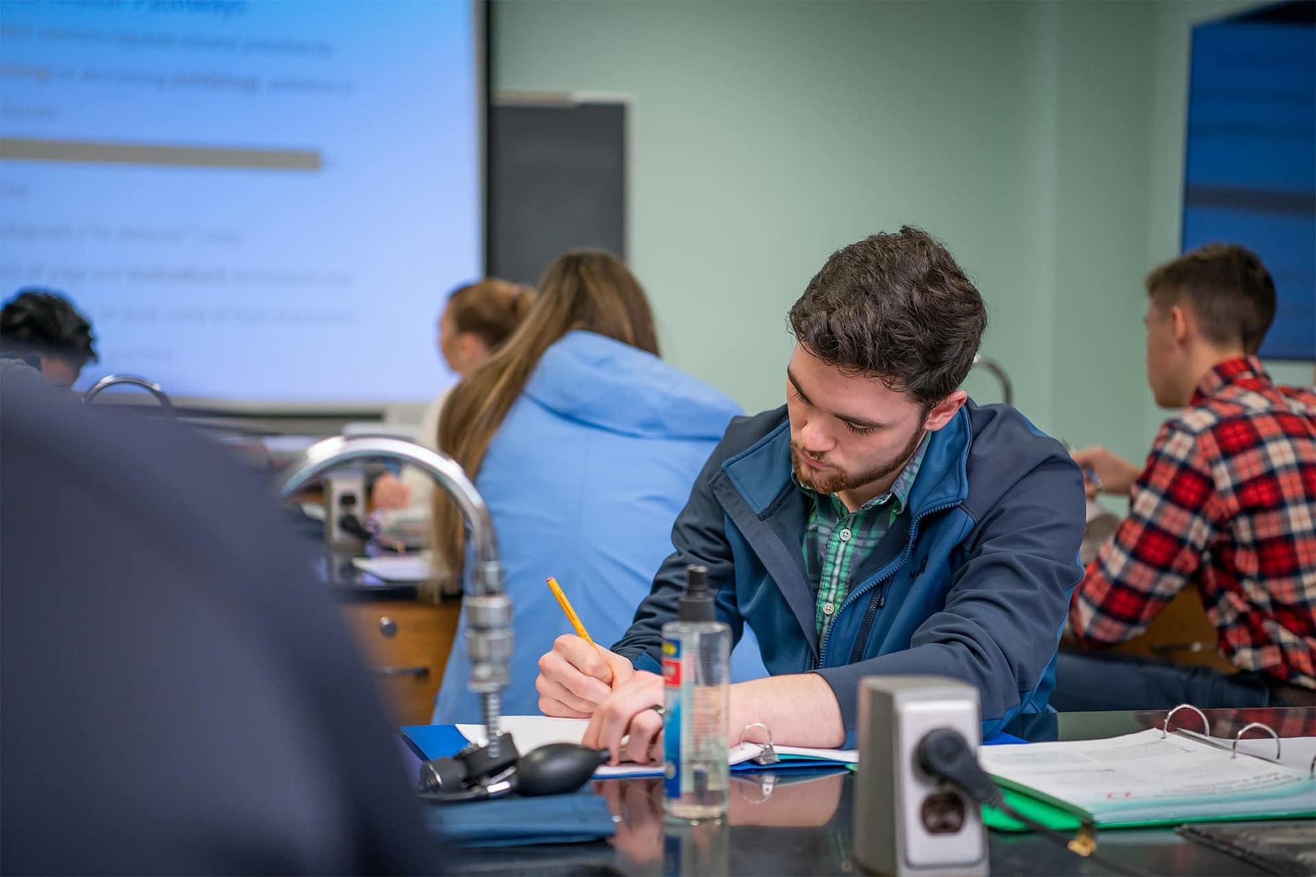 Male student sitting at a lab table and writing in a notebook at the start of the new semester.