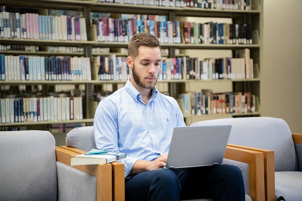 Andrew Malack typing on a laptop in the library. 