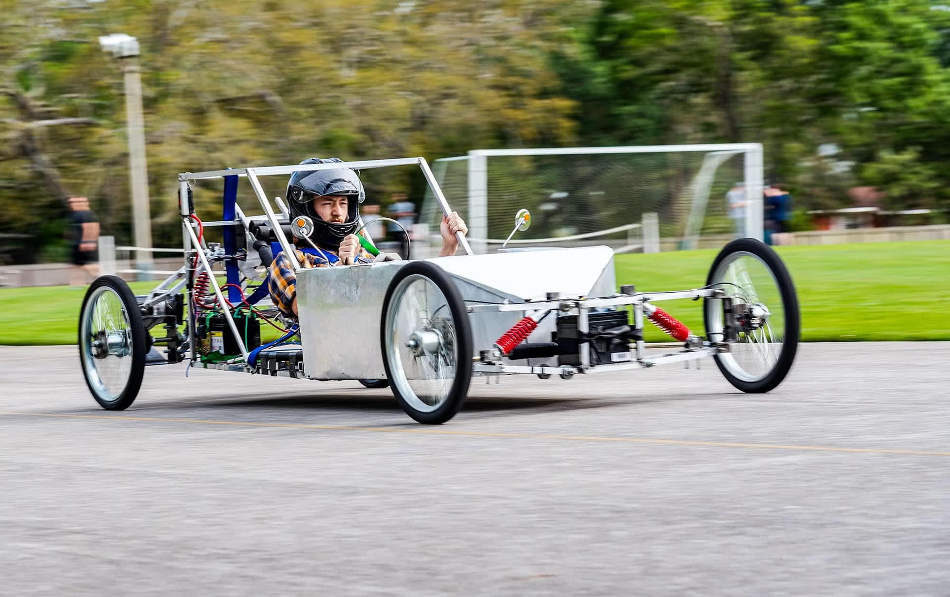 Student racing in a silver electric vehicle and wearing a helmet. 