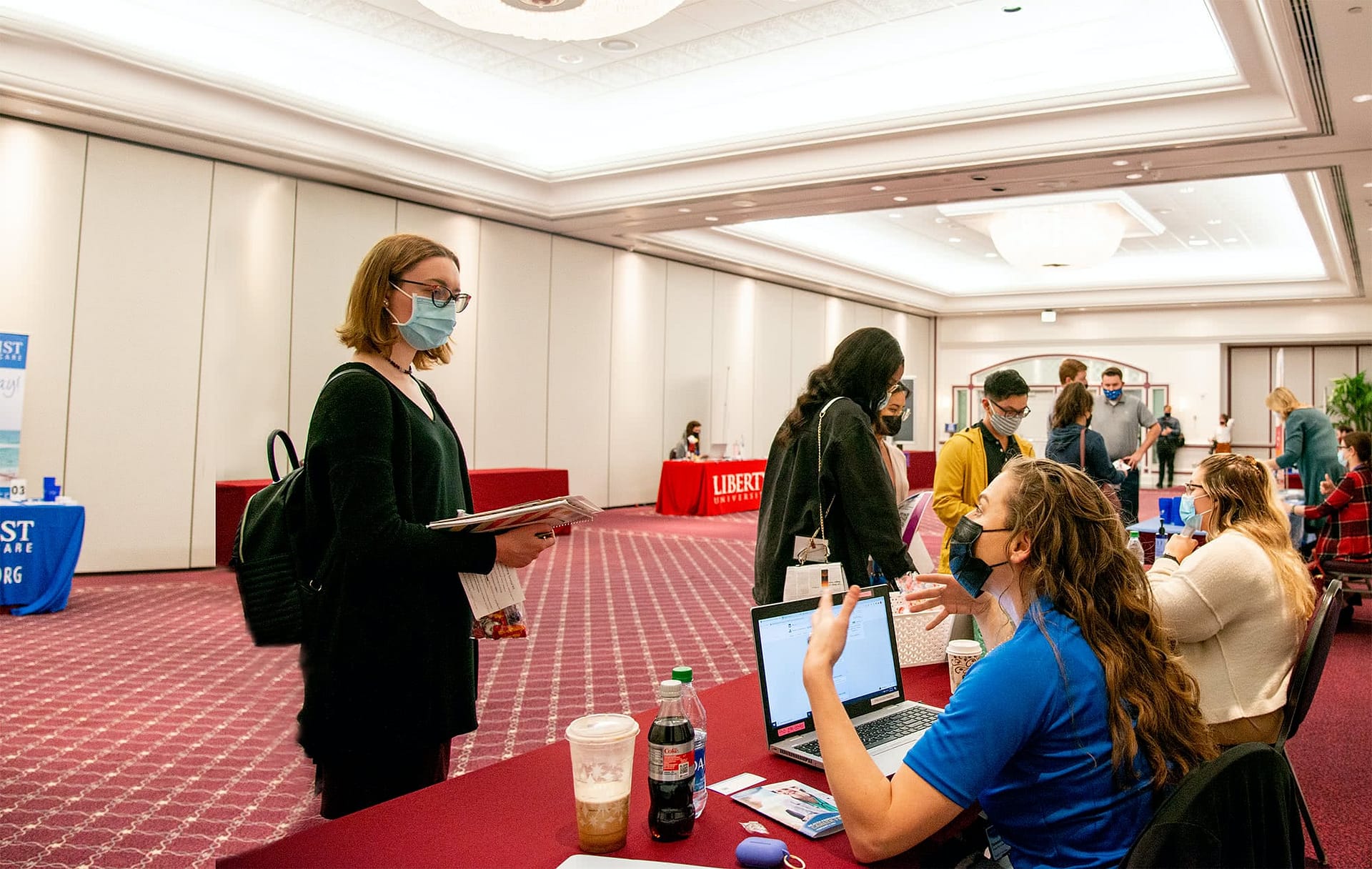 Female student standing at a booth during the Health Professions Career Fair and speaking with a woman sitting behind the booth.