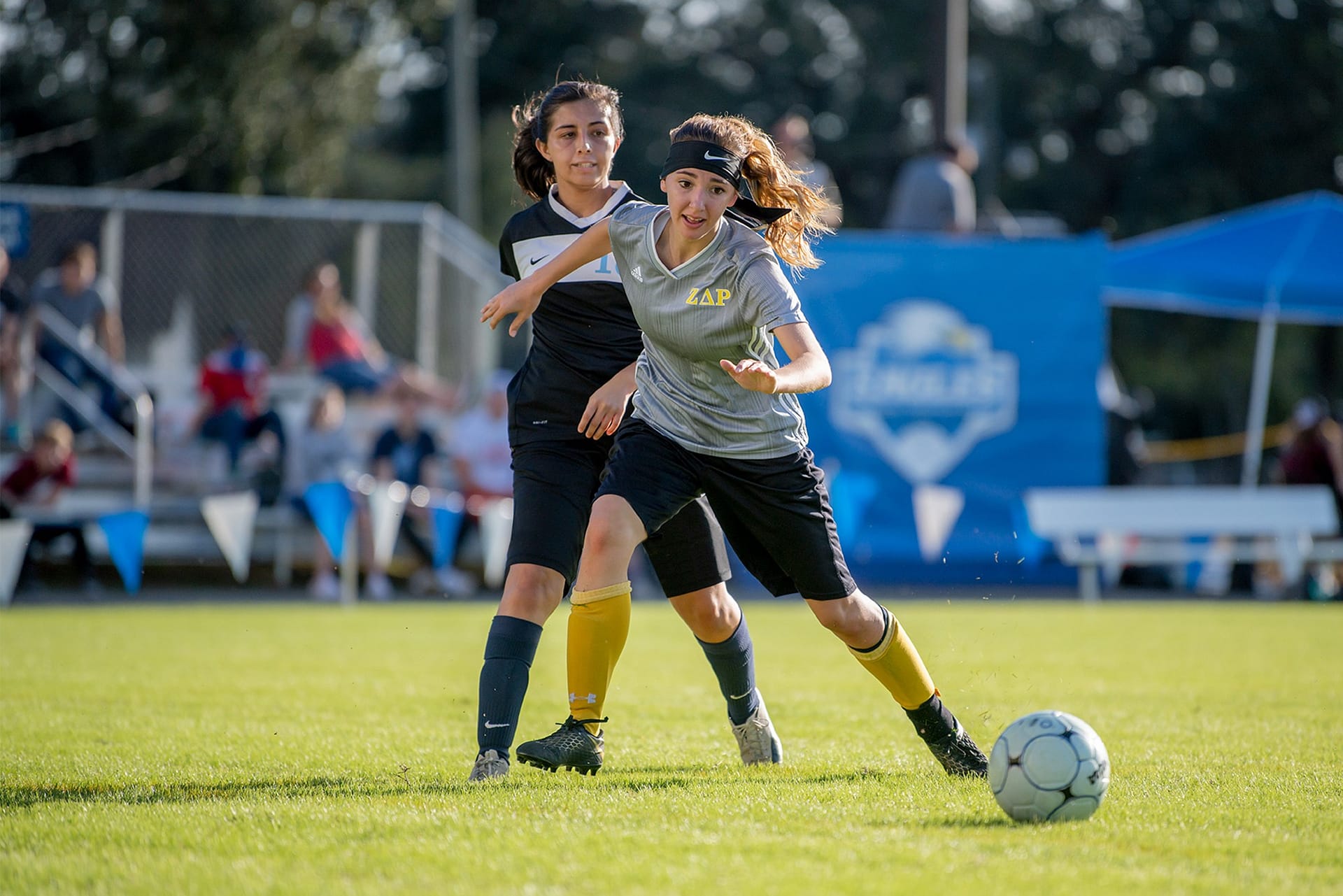 Two female student soccer players chasing toward a soccer ball on Eagle's Field.