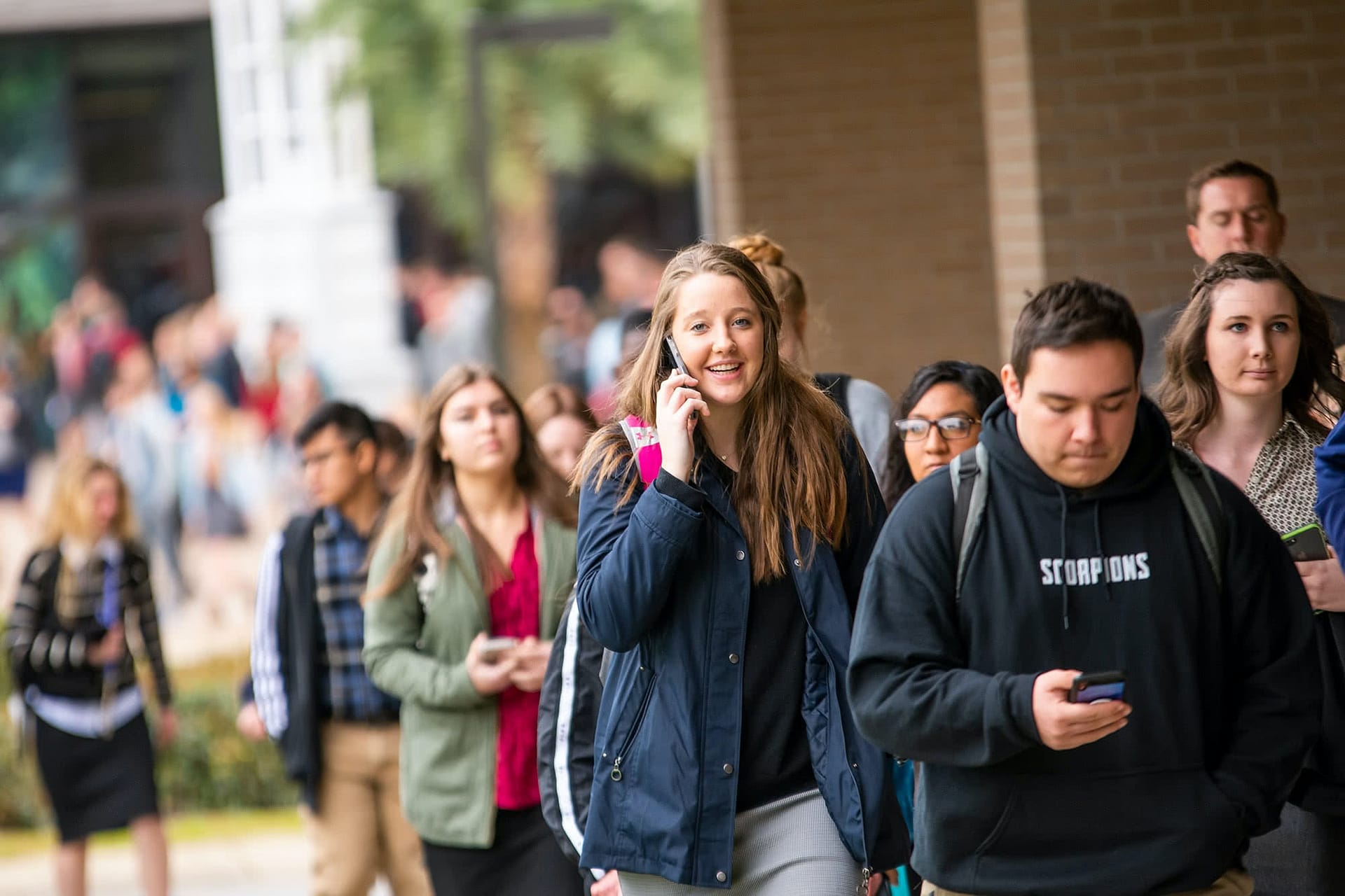 Female student talking on the phone and walking in a group of other students.
