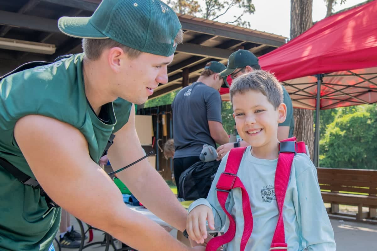 Team Leader at Camp O' the Pines helps a camper with a safety harness