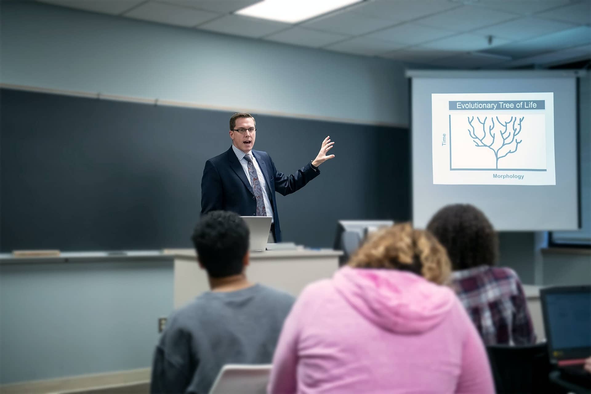 Male interterm teacher instructing students and showing a slideshow.