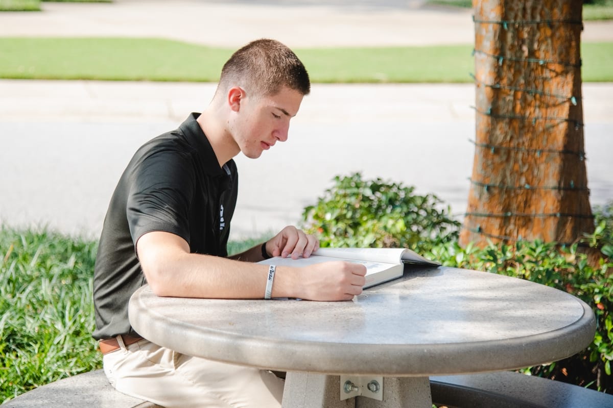 PCC guy reading a book at a table outside