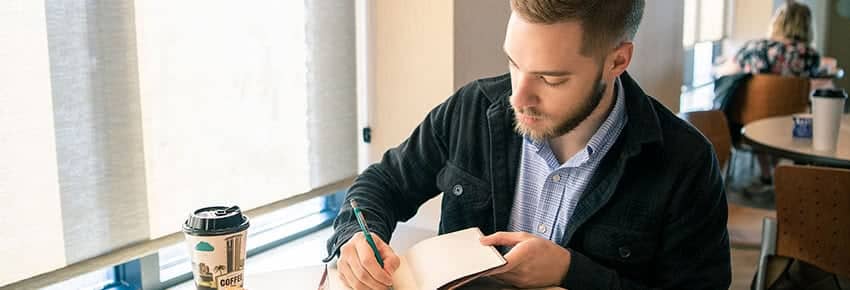 Graduate Assistant writing in a notebook in the PCC Commons. 