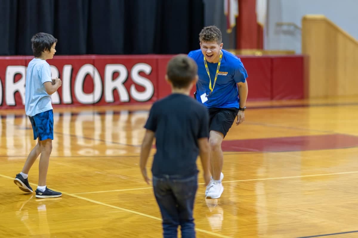 Discover Day Camp team leader plays with campers in the gym