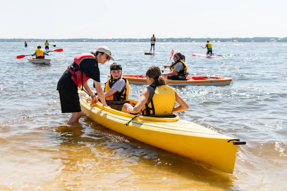 Team Extreme team leader helps campers in a kayak at West Campus