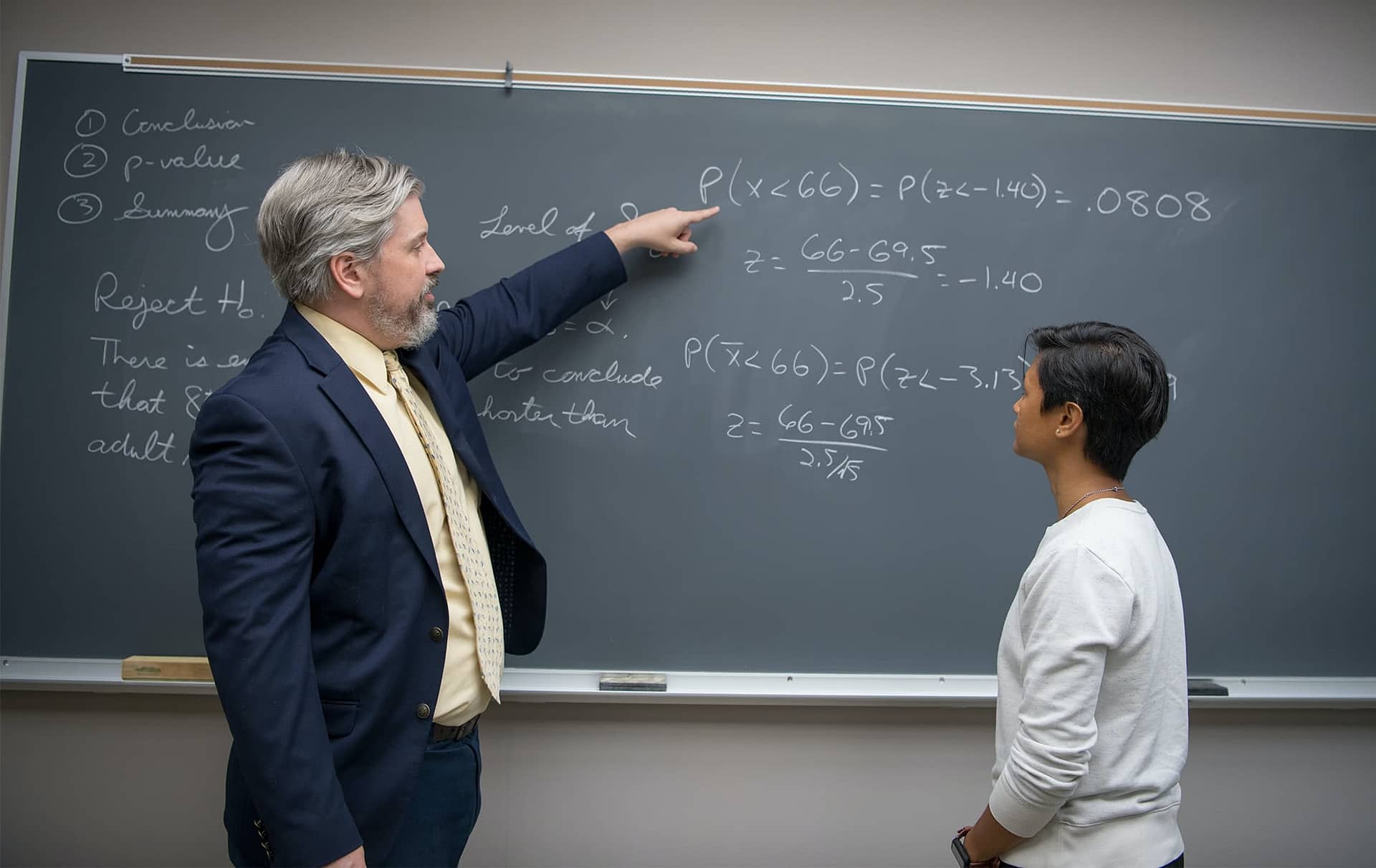 Professor pointing to the chalkboard and showing an equation to a female graduate student. 