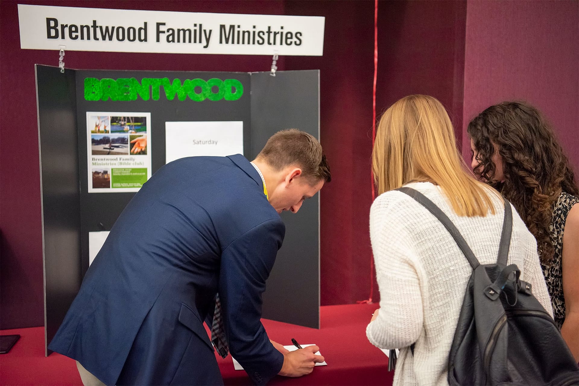 Two girls talk to a male studnet about volunteering with Brentwood Family Ministries