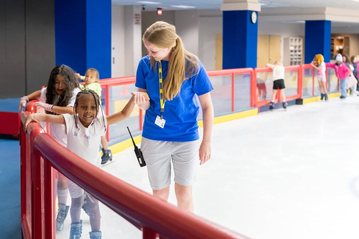 Sports Center Day Camp team leader helps a camper ice skate