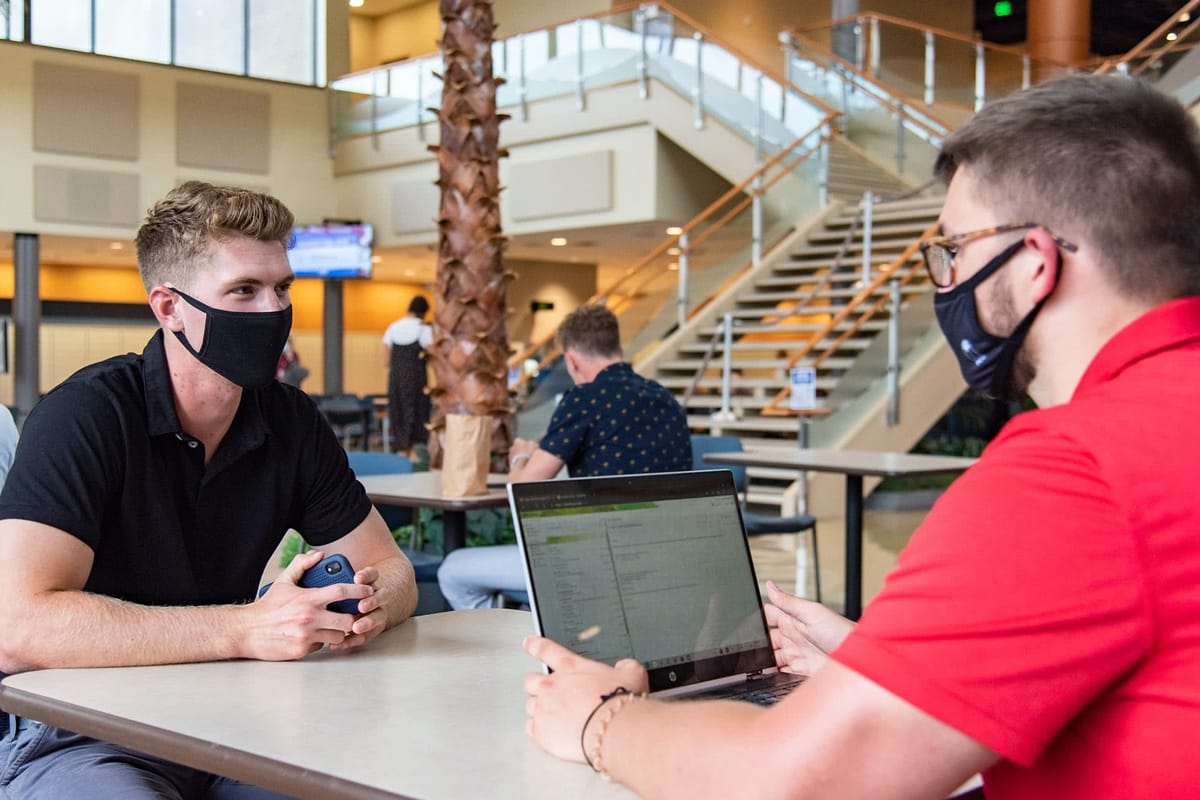 Two PCC guys wearing masks and sitting at a table in the Commons