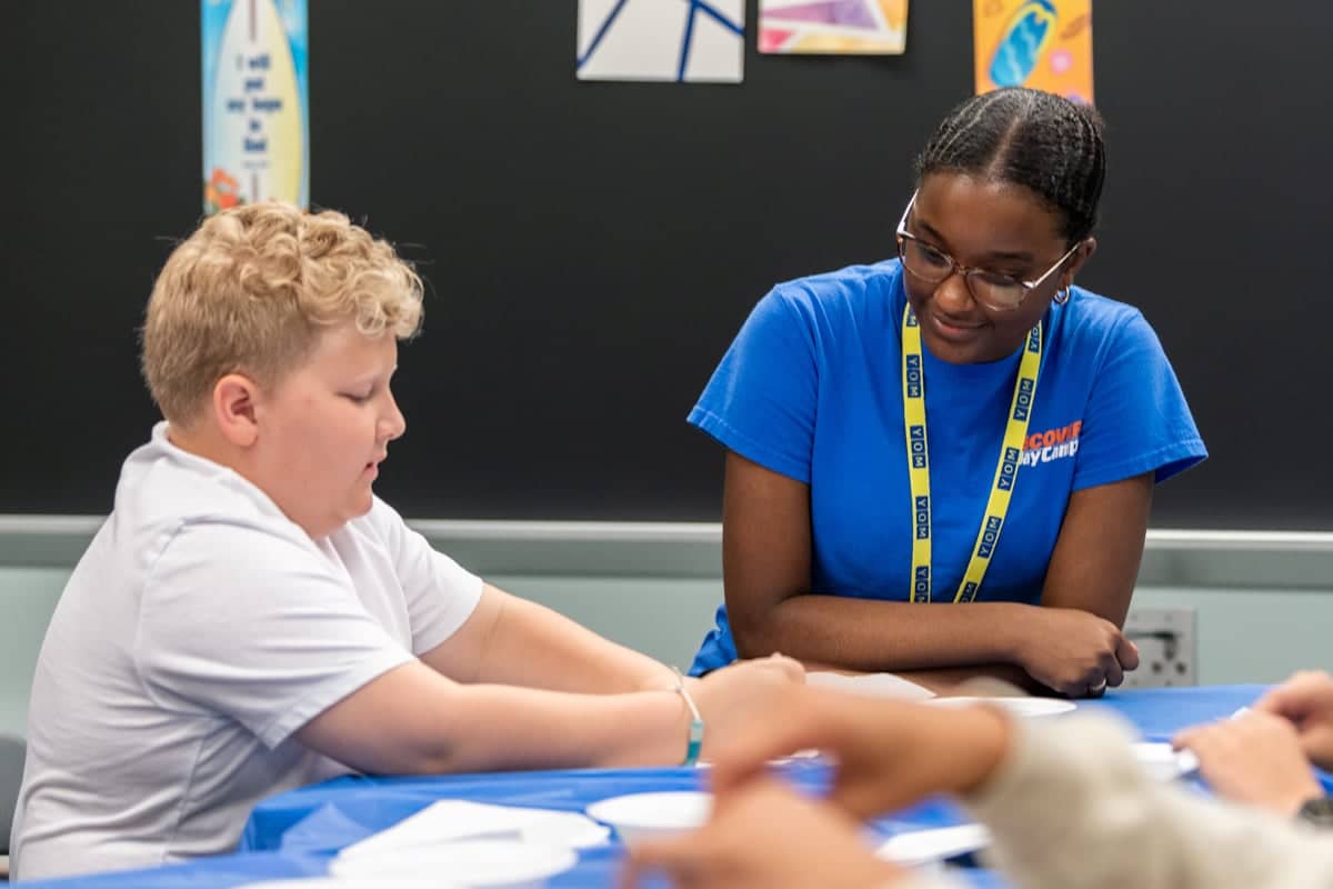 Discover Day Camp team leader works with a camper on a project