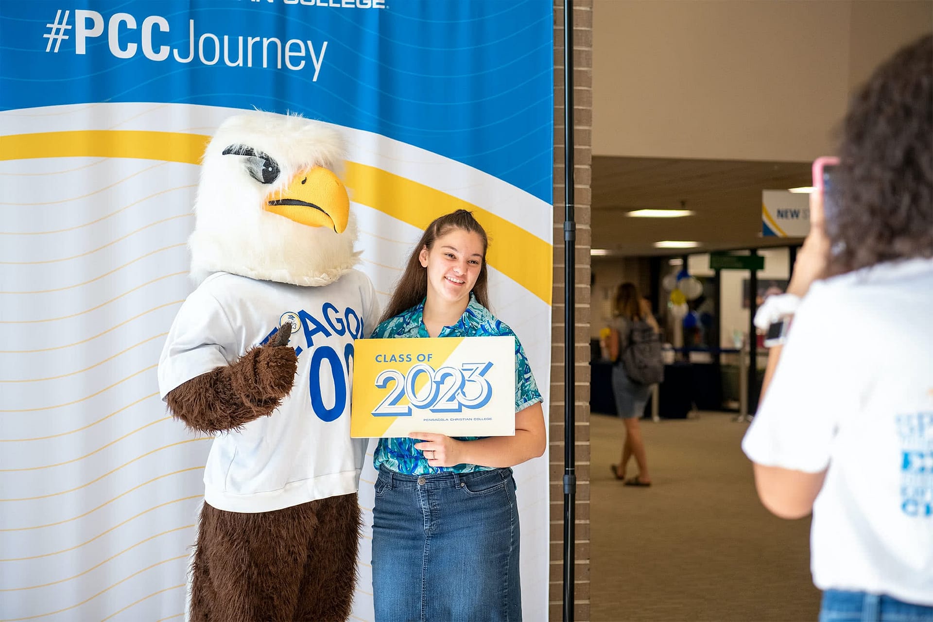 A new freshman poses with Eagor holding a sign that says "class of 2023"