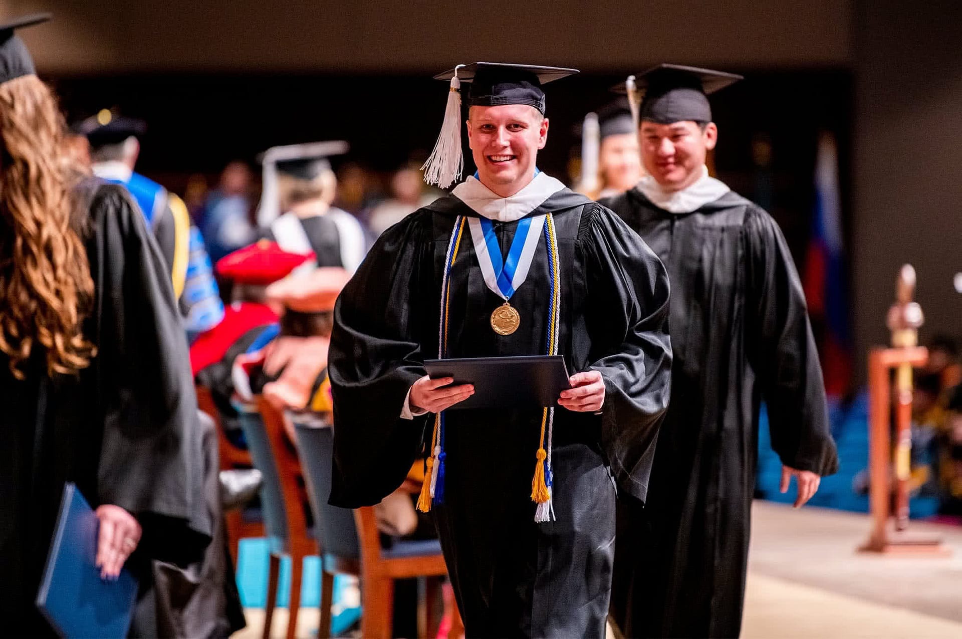 Male graduate walking across Crowne Centre stage