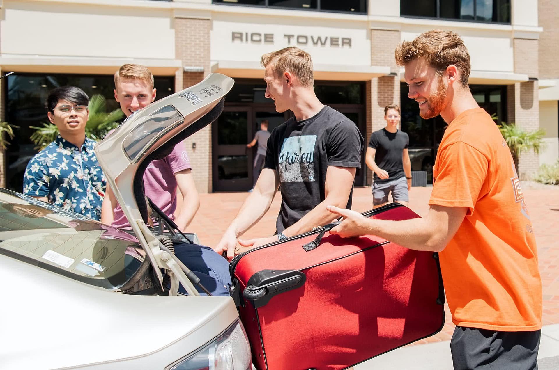 Male PCC students putting suitcase into the trunk of a silver car.